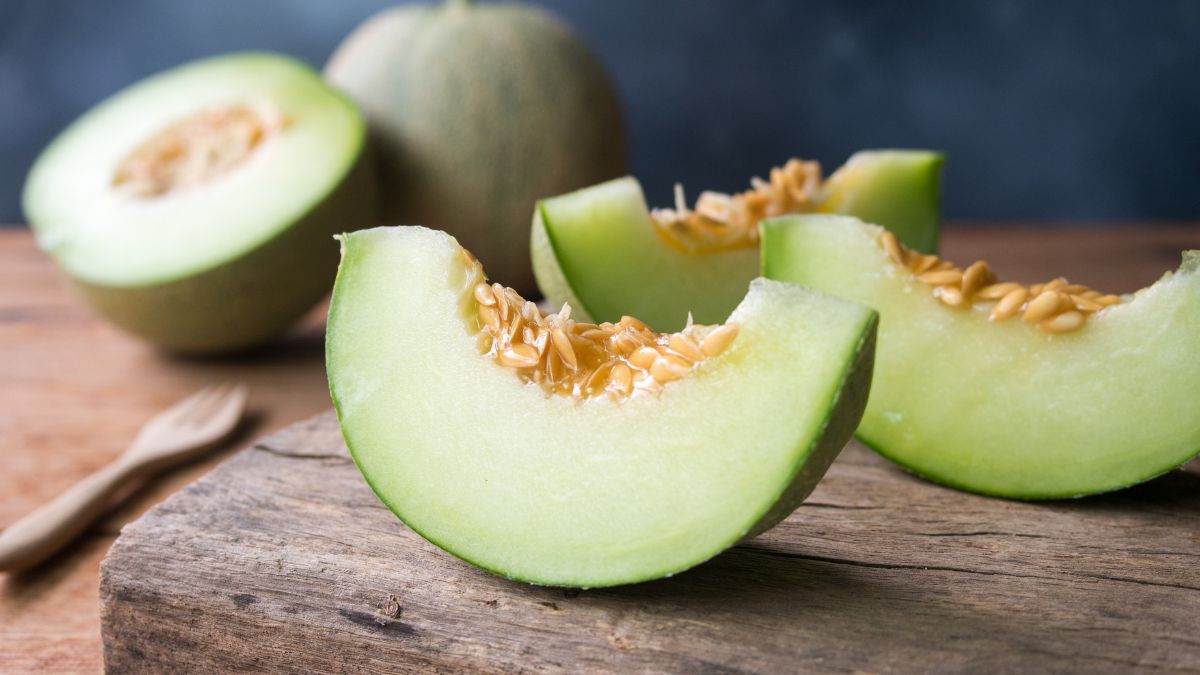 Friss sárgadinnye szeletek, mellette egész dinnye, fából készült kanál.