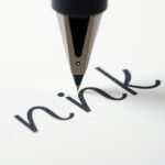 Golyóstoll írás közben, betűk a papíron.