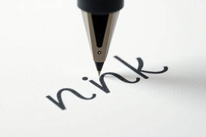 Golyóstoll írás közben, betűk a papíron.