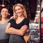 Két nő mosolyog egy kávézóban, üzletnyitási tanácsokat megjelenítve.
